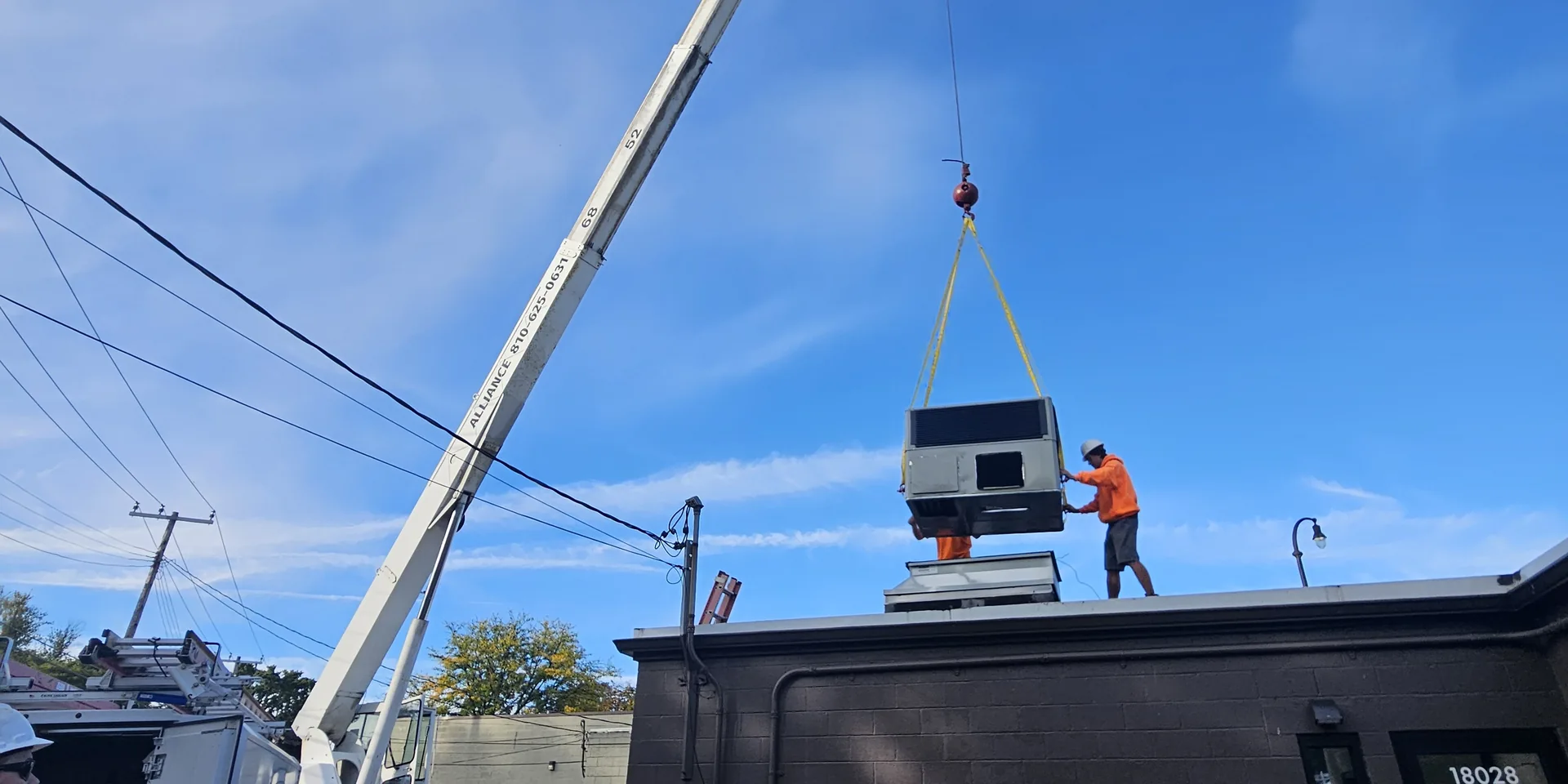 Technician guiding a new commercial packaged rooftop air conditioning unit onto its roof curb